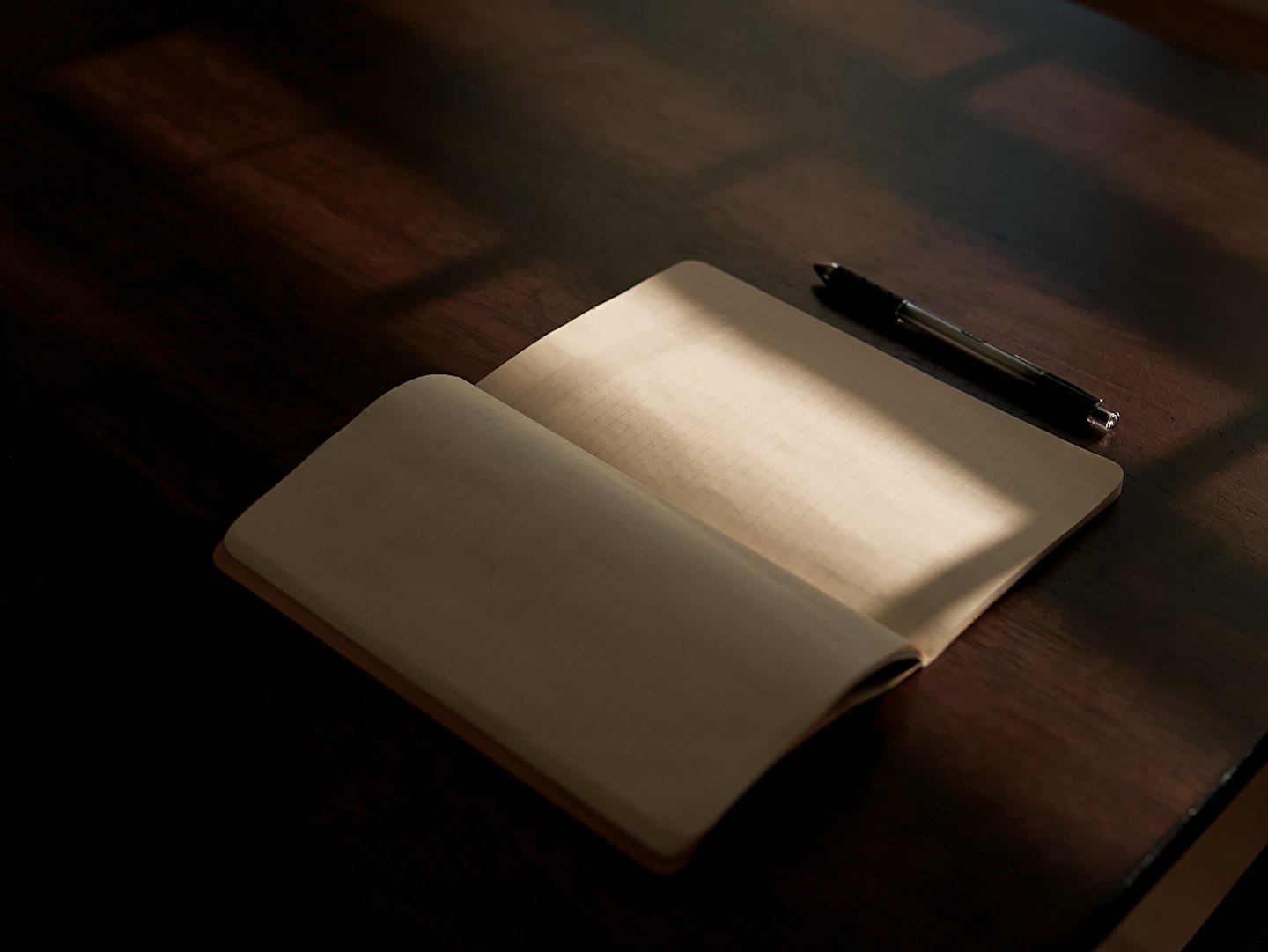 Un cuaderno abierto y un bolígrafo sobre un escritorio de madera.